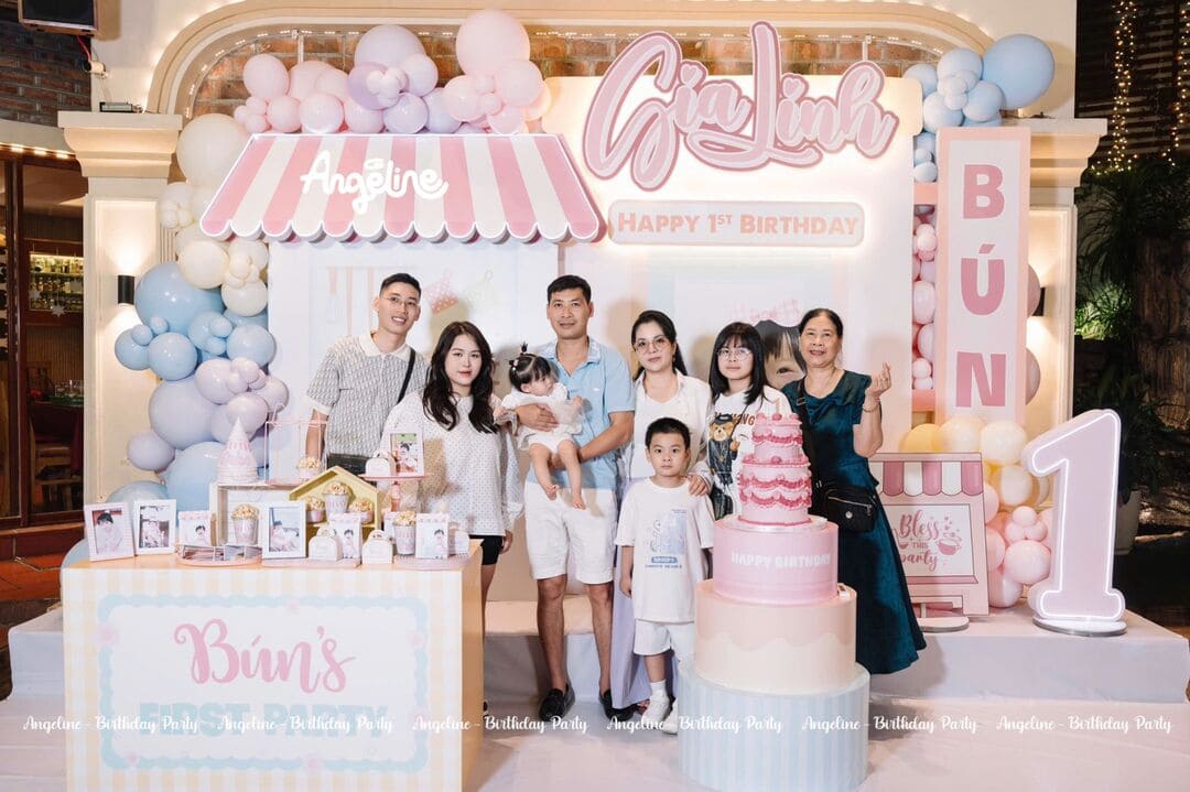 Buổi tiệc sinh nhật 1 tuổi bé Gia Linh là một ngày thật đặc biệt, nơi cả gia đình cùng nhau lưu lại những khoảnh khắc hạnh phúc đầu tiên của con yêu. Tất cả được Angeline Decor chuẩn bị tỉ mỉ với cảm hứng từ tiệm bánh pastel nhỏ xinh, mang tông hồng – xanh baby nhẹ nhàng, dễ thương. Không gian ngọt ngào như bước vào thế giới bánh kem và kẹo ngọt, nơi mọi chi tiết đều toát lên sự tinh tế và yêu thương. Đây không chỉ là một buổi tiệc, mà là món quà ba mẹ dành riêng cho thiên thần nhỏ tròn 1 tuổi – bé Gia Linh. ________________________________________ Concept & Tone chủ đạo: Mini Bakery – Tiệm bánh dành riêng cho Bún Concept “Mini Bakery” mang hơi thở ngọt ngào, tinh khôi và ấm áp. Tông hồng pastel, xanh baby và vàng kem nhẹ tạo nên bức tranh trong trẻo, dễ chịu. Mỗi chi tiết nhỏ đều được Angeline Decor thiết kế như một mảnh ghép cảm xúc – mềm mại, hài hòa và đầy nữ tính. Bước vào buổi tiệc sinh nhật 1 tuổi bé Gia Linh, mọi người như lạc vào một tiệm bánh mini xinh xắn, nơi ánh sáng, màu sắc và hương vị hòa quyện. Cảm giác ấm áp lan tỏa khắp không gian, khiến bất kỳ ai cũng mỉm cười khi nhìn thấy ánh mắt rạng rỡ của bé. ________________________________________ Backdrop & Bàn tiệc – Hai khu vực nổi bật nhất Backdrop chính – điểm nhấn ngọt ngào Backdrop được thiết kế với tên “Gia Linh” và dòng chữ Happy 1st Birthday, kết hợp dải bóng bay pastel và bảng số 1 phát sáng nổi bật. Hình ảnh bé được in xinh xắn đặt giữa phông nền pastel nhẹ, tạo nên góc chụp hình “đốn tim” khách mời. Phía trước là bàn gallery trưng bày ảnh bé trong năm đầu đời cùng bánh kẹo và phụ kiện mini. Mỗi bức ảnh là một kỷ niệm – từ nụ cười đầu tiên, ánh mắt tò mò cho đến khoảnh khắc bé tập đi. Tất cả hòa quyện tạo nên câu chuyện nhỏ đầy cảm xúc. Bàn tiệc – nơi sum vầy ấm áp Bàn tiệc được bố trí tinh tế với ribbon hồng trên ghế, hoa tươi nhỏ xinh làm điểm nhấn. Tông nâu – trắng – xanh lá nhẹ mang lại cảm giác tự nhiên, thanh thoát. Không gian mở đón ánh sáng tự nhiên giúp buổi tiệc thêm gần gũi, thân mật. Dưới ánh nắng nhẹ, bánh sinh nhật pastel nhiều tầng trở thành trung tâm của mọi ánh nhìn. Mọi chi tiết đều được sắp xếp để mang lại trải nghiệm thoải mái, ấm áp và đáng nhớ. ________________________________________ Chi tiết trang trí ấn tượng Bánh sinh nhật pastel nhiều tầng Chiếc bánh sinh nhật của bé Gia Linh được thiết kế đồng điệu với backdrop. Từng tầng bánh là sự pha trộn tinh tế giữa sắc hồng, kem và xanh baby, điểm xuyết những bông hoa nhỏ và topper mang tên bé. Bên cạnh là những chiếc cupcake, bánh macaron và kẹo dẻo nhỏ được sắp khéo léo trên bàn gỗ, tạo cảm giác vừa ngon mắt vừa chân thực. Mọi người không chỉ chụp ảnh cùng bánh mà còn ngỡ như đang thưởng thức hương vị ngọt ngào của tiệm bánh thật sự. Bàn gallery – nơi kể câu chuyện đầu đời Mỗi khung ảnh của bé trên bàn gallery là dấu mốc đáng nhớ. Angeline Decor chọn cách trang trí tối giản với đèn vàng ấm, lọ hoa nhỏ và phụ kiện handmade. Khi nhìn ngắm từng bức hình, ai cũng cảm nhận được tình yêu thương vô bờ của ba mẹ dành cho bé. Đèn LED chữ & số – điểm sáng của buổi tiệc Đèn LED chữ “Gia Linh” và số “1” được bố trí nổi bật, ánh sáng vàng nhẹ giúp không gian thêm lung linh. Ánh đèn không chỉ làm nổi bật chủ đề tiệm bánh, mà còn giúp mọi khung hình thêm rạng rỡ, ấm áp và sống động. ________________________________________ Cảm xúc & ý nghĩa của buổi tiệc Buổi tiệc sinh nhật 1 tuổi bé Gia Linh là kỷ niệm đầu tiên đánh dấu hành trình khôn lớn của con. Đó là khi ba mẹ nhìn con thổi nến, ông bà mỉm cười hạnh phúc, và cả gia đình cùng nhau hát vang bài “Happy Birthday” trong không gian ngập tràn yêu thương. Với Angeline Decor, mỗi buổi tiệc không chỉ là trang trí đẹp mắt, mà là cách gửi gắm yêu thương qua từng chi tiết. Chúng tôi tự hào được đồng hành cùng ba mẹ tạo nên khoảnh khắc đầu tiên đầy ý nghĩa cho bé – nơi mọi kỷ niệm được thắp sáng bằng cảm xúc và sự tận tâm. ________________________________________ Angeline Decor – Biến buổi tiệc nhỏ thành kỷ niệm lớn Angeline Decor luôn mong muốn mang đến những buổi tiệc đẹp – tinh tế – ý nghĩa dành cho các bé. Mỗi concept được chúng tôi thiết kế đều có câu chuyện riêng, phù hợp với tính cách, sở thích và mong muốn của gia đình. Nếu bạn đang lên kế hoạch tổ chức tiệc sinh nhật 1 tuổi cho bé yêu, hãy để Angeline Decor giúp bạn tạo nên không gian mơ ước. Từ ý tưởng, thiết kế, thi công cho đến chụp ảnh và hoàn thiện decor, tất cả sẽ được thực hiện trọn gói – chuyên nghiệp và đầy tâm huyết.