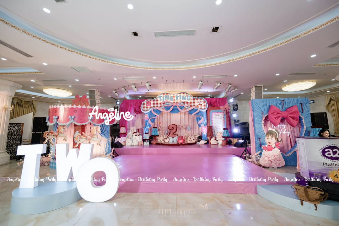Sân khấu Ting Ting's Wonderland với bảng tên caro, rèm hồng xanh và bánh sinh nhật trung tâm